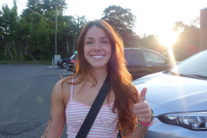 girl in striped dress in front of car giving a thumbs up