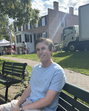 A young white man sits on a bench in front of a historic building