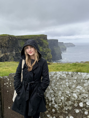 A young white woman in a black raincoat standing near the cliffs in Ireland