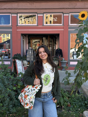 A young woman posing and smiling outside a small shop at the farmer's market in Troy NY.  