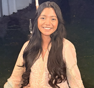 a girl with long black hair sitting and smiling at the camera